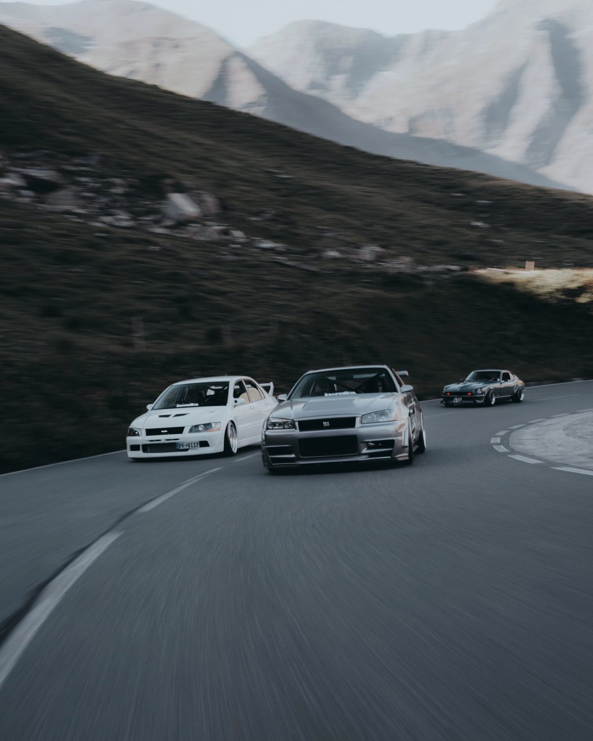 Skyline R34, Evo and classic Datsun rolling through an alpine curve with motion blur