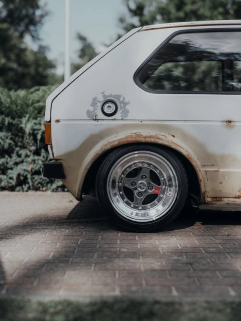 Rear quarter of a patinated white Golf Mk1, rusty arches over polished Tramont split-rim wheels