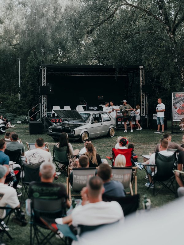 Silver Golf Mk1 with its bonnet open in front of the VolxZone stage, the crowd watching from camping chairs on the grass