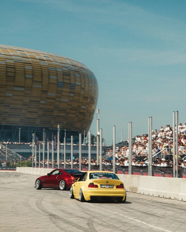 Red Nissan 350Z and yellow BMW E46 M3 drifting side by side on the Ultrace Parking Area with a crowd and Polsat Plus Arena behind