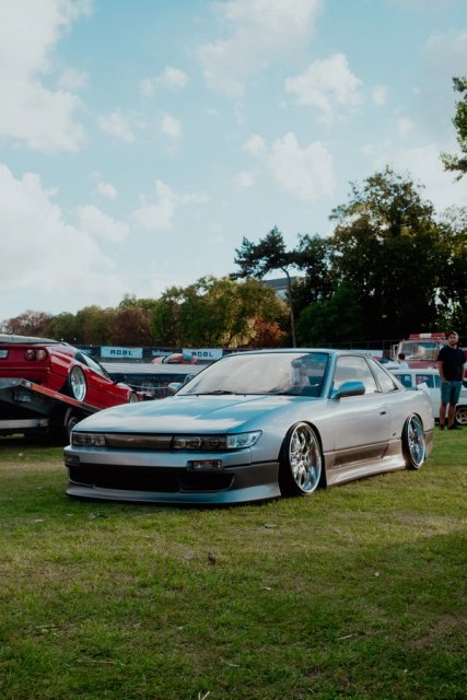 A silver Nissan Silvia S13 on the grass, a red Ferrari parked behind it