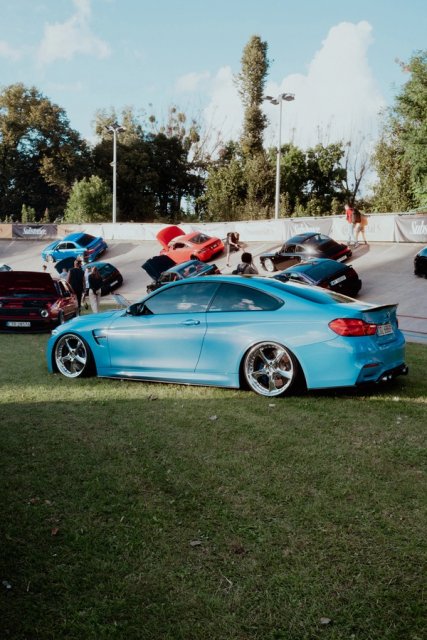 A pale blue BMW M4 in profile against the white wall of the velodrome