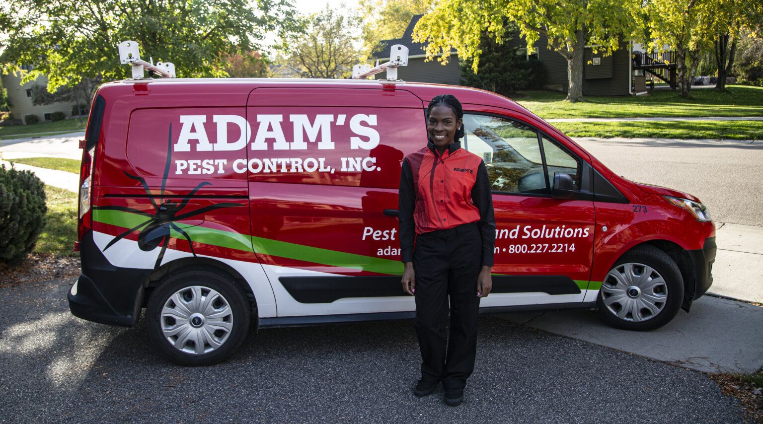 Adam’s Pest Control technician smiling outside a residential home near branded service van