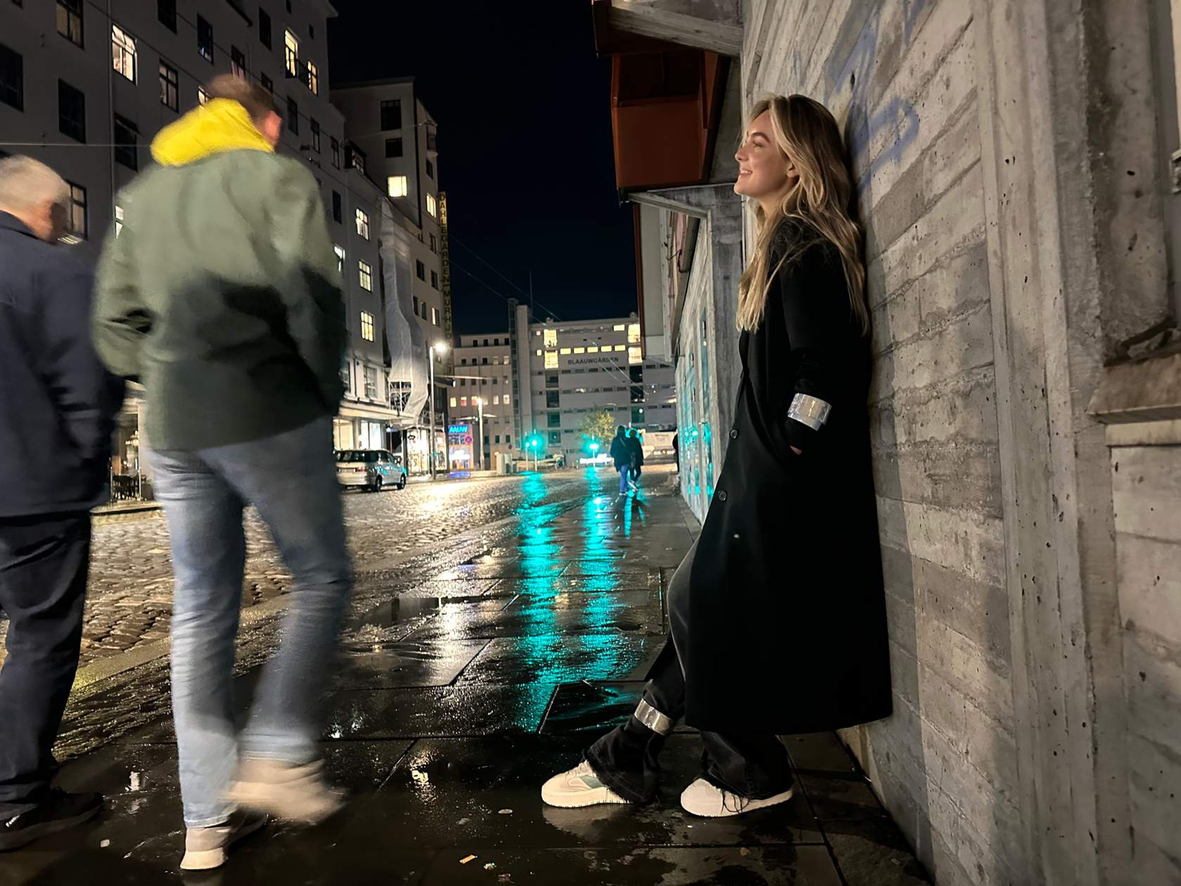 Ungdom, kvinne som står inntil en vegg om kvelden med slapwraps på arm og ben på fortau i gatebilde
