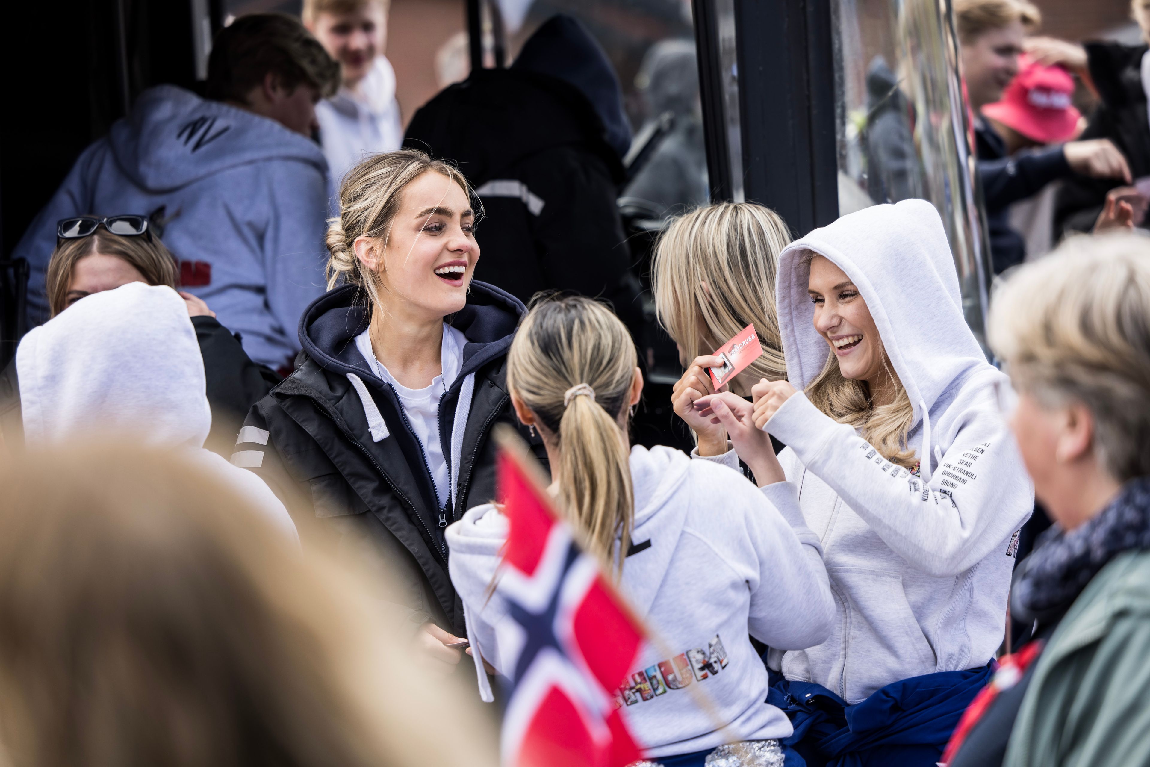 Tre russ som smiler til hverandre. Den ene holder et russekort