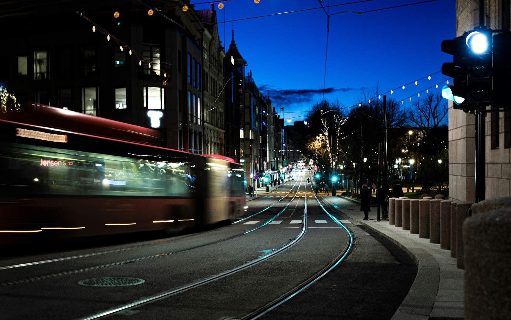 Mørk gate med trikkeskinner, trafikklys og en buss som passerer