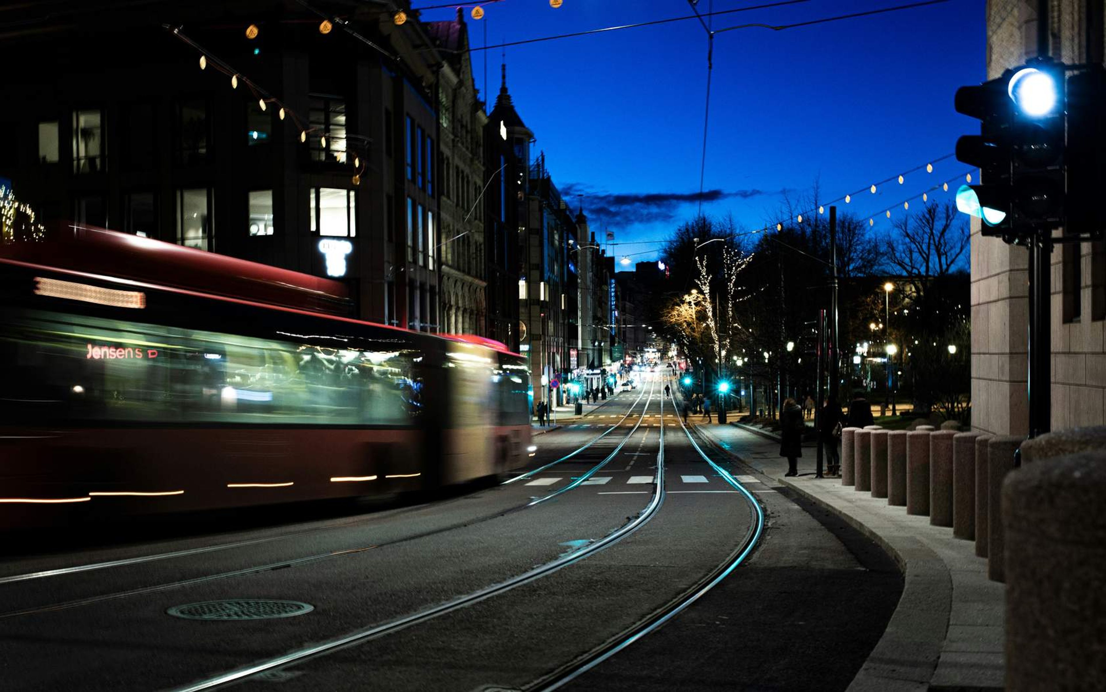 Mørk gate med trikkeskinner, trafikklys og en buss som passerer
