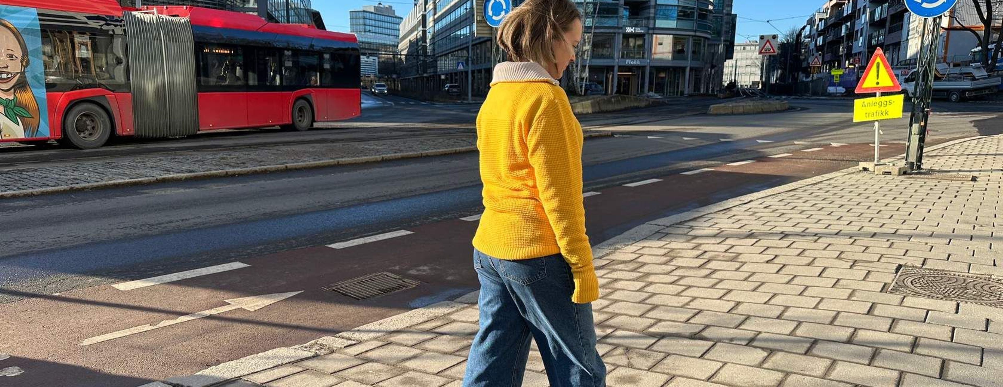 Kvinne som går på fortauet med en buss som kjører forbi