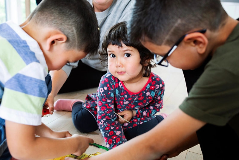 Familiekontakt sitter i bakgrunnen, og 3 barn sitter i forgrunnen og pusler puslespill.