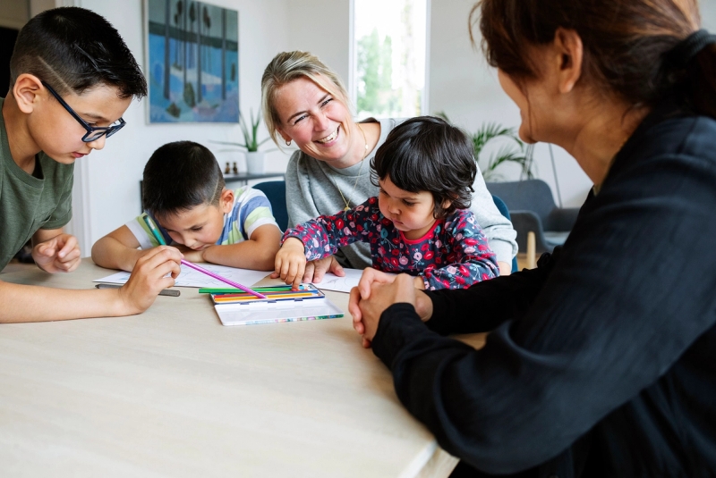 Familiekontakt og mor med 3 barn sitter ved et bord og tegner.