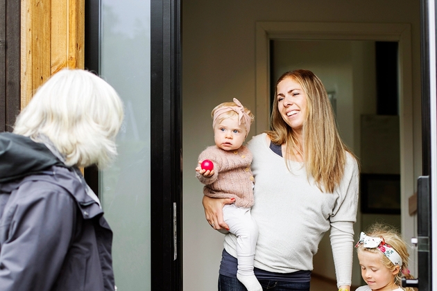 Familiekontakt med ryggen til i døråpning. Mor og 2 døtre innenfor døren.