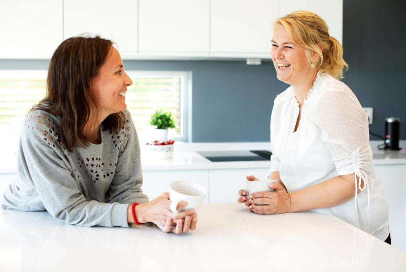 Familiekontakt og mor snakker sammen ved kjøkkenbenk.
