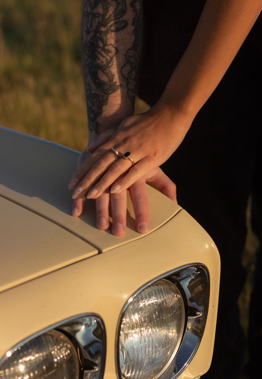 Two hands with rings resting on the hood of a vintage car