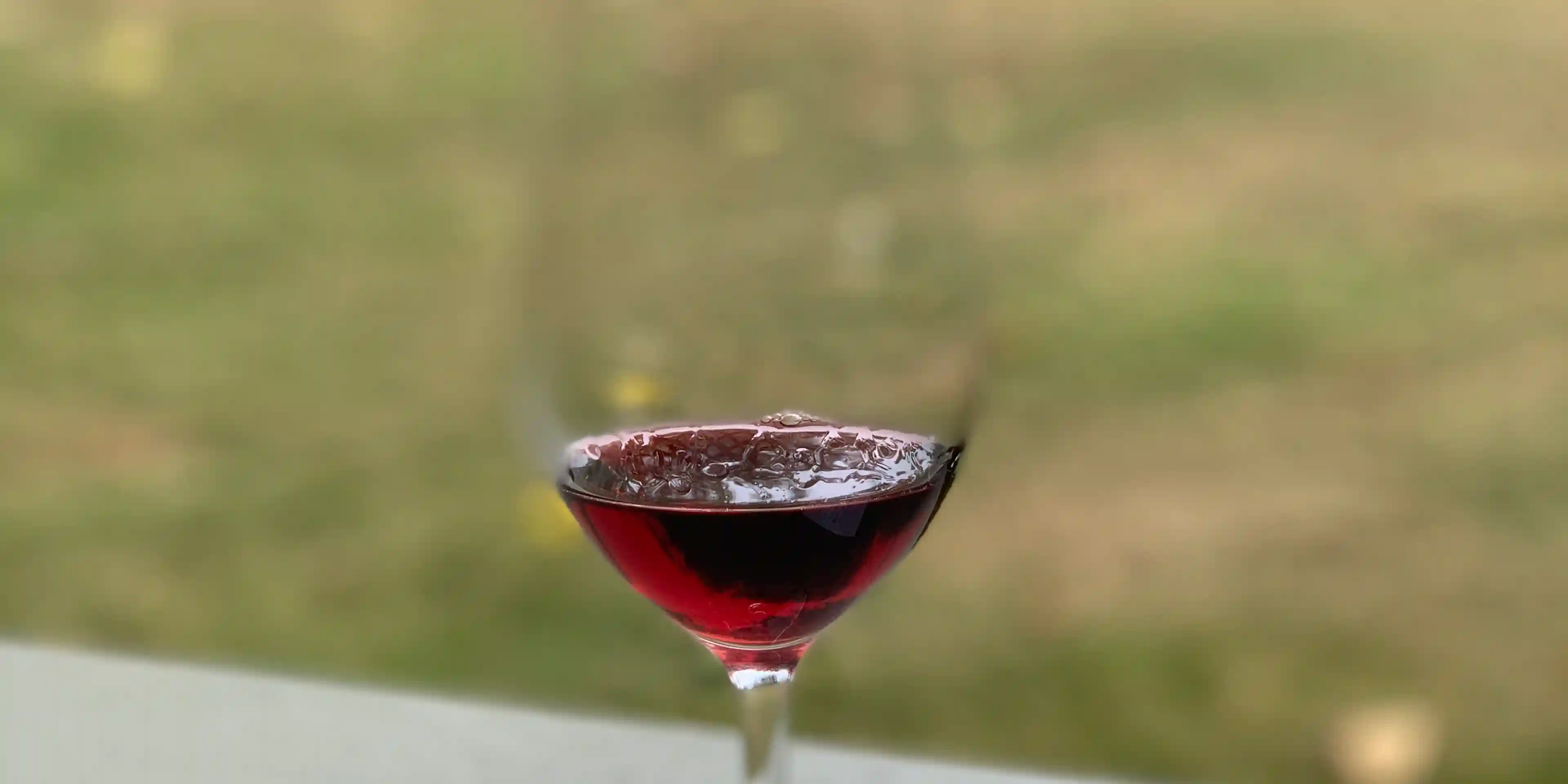Shot of a glass of red wine, with a lawn in the background
