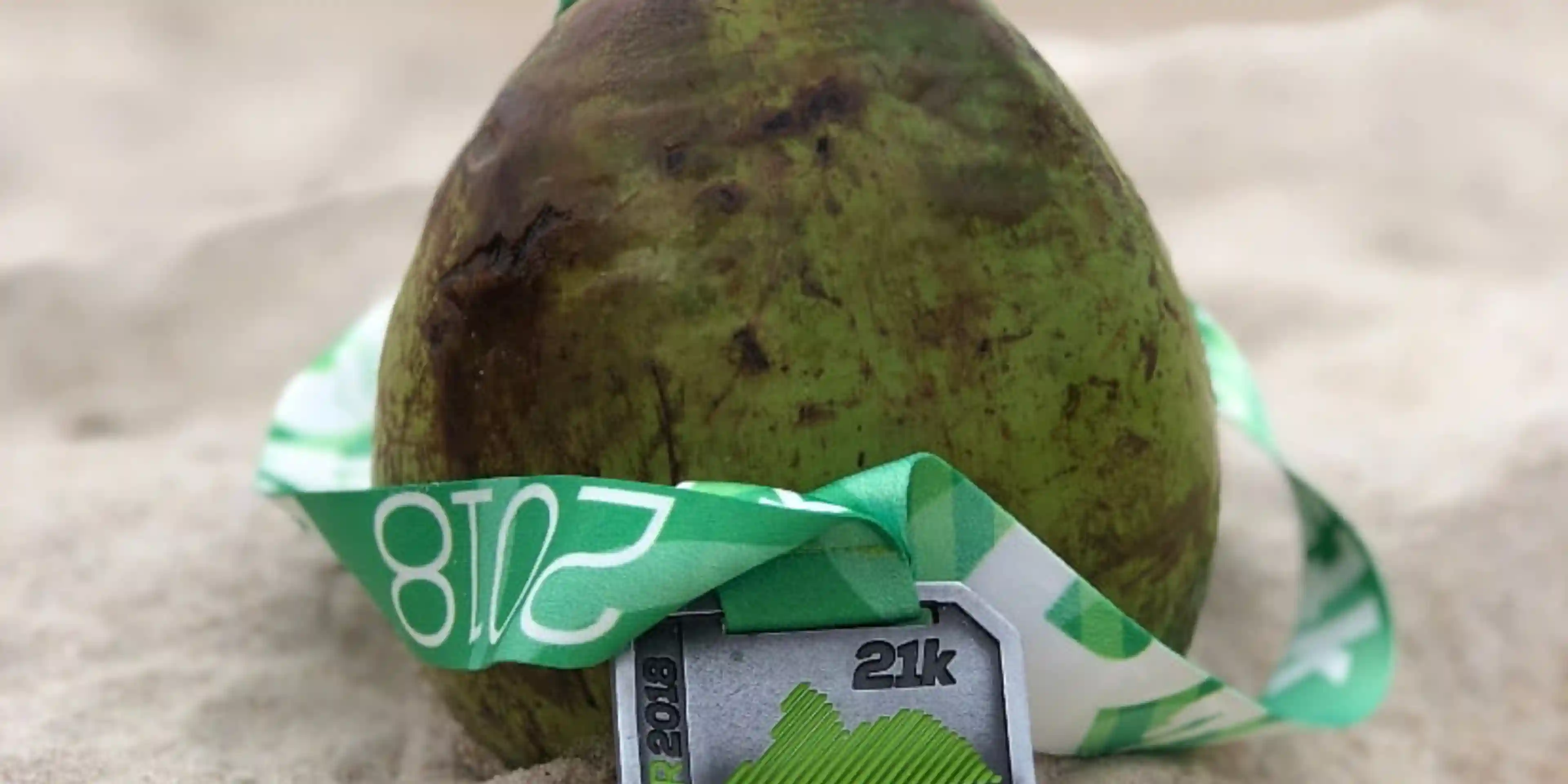 This picture shows a fresh coconut with a straw in it, with a 2018 Maratona do Rio 21km race medal wrapped around it