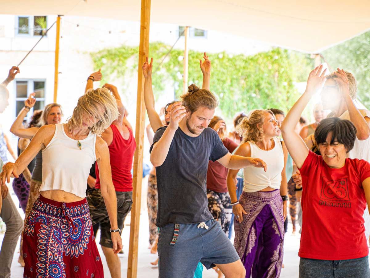 Een groep mensen danst samen onder een zeil in het zonlicht.