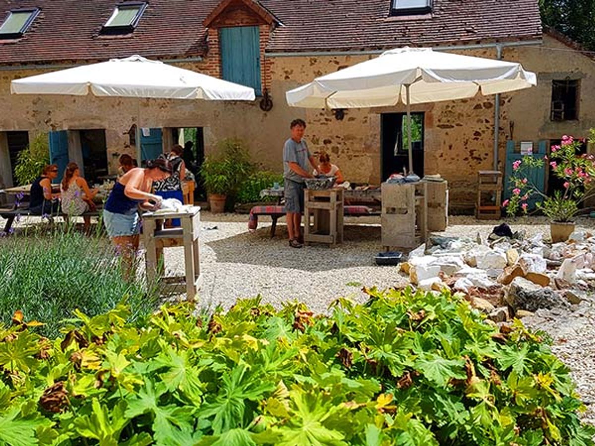 Het binnenplein van Le Moulin met parasols en deelnemers aan het werk in de tuin