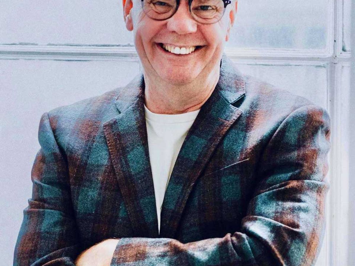 Portret van Jon Skelton Pearson, glimlachend met een geruite jas en bril