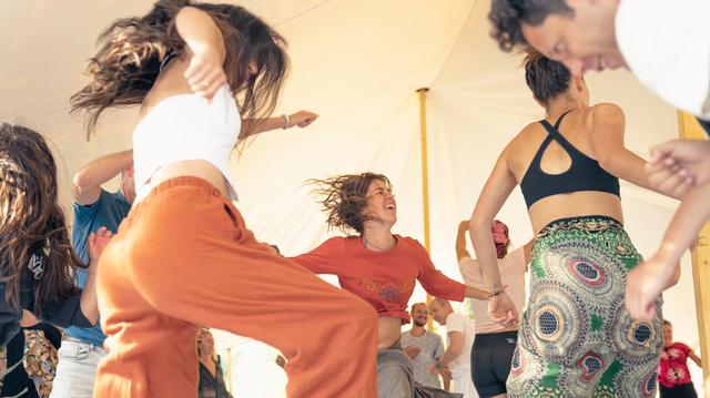 Een groep danst vol energie in een lichte tent.