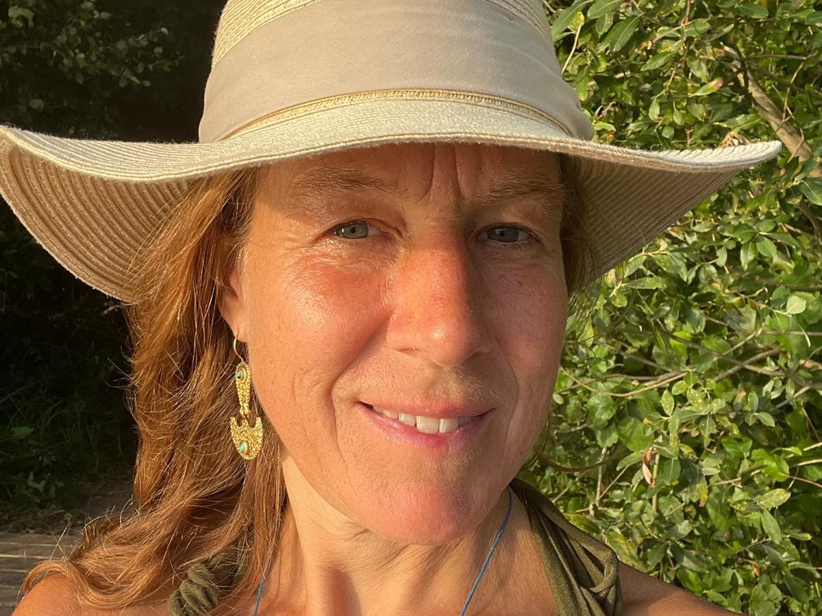 Mascha Löschmann buiten in de natuur, met een lichte zonnehoed en groene bladeren op de achtergrond
