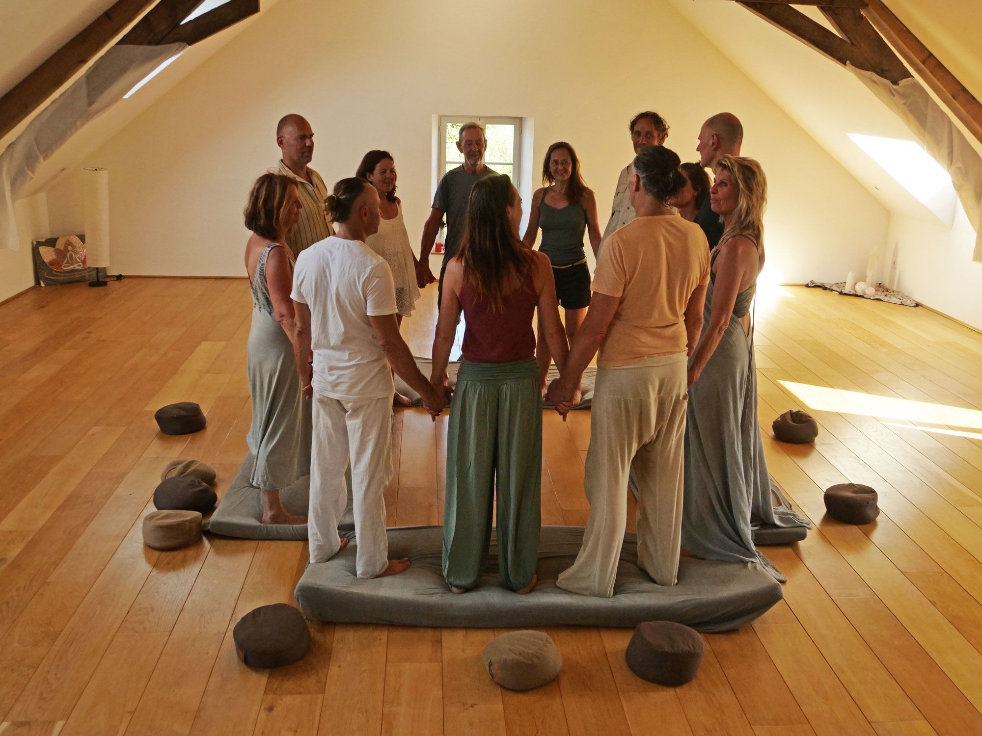 Een groep staat hand in hand in een kring in een lichte zaal met houten balken