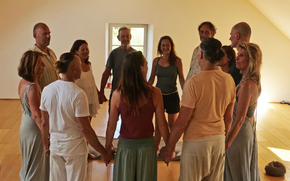 Een groep staat hand in hand in een kring in een lichte zaal met houten balken