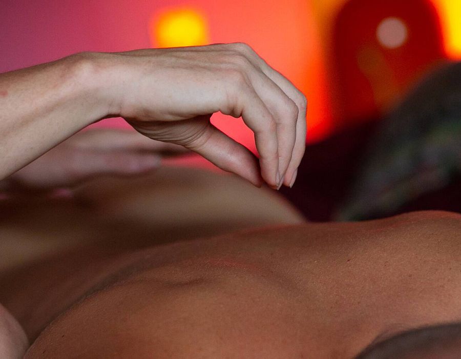 Hand zweeft zacht boven de borst van een liggende man bij warm sfeerlicht