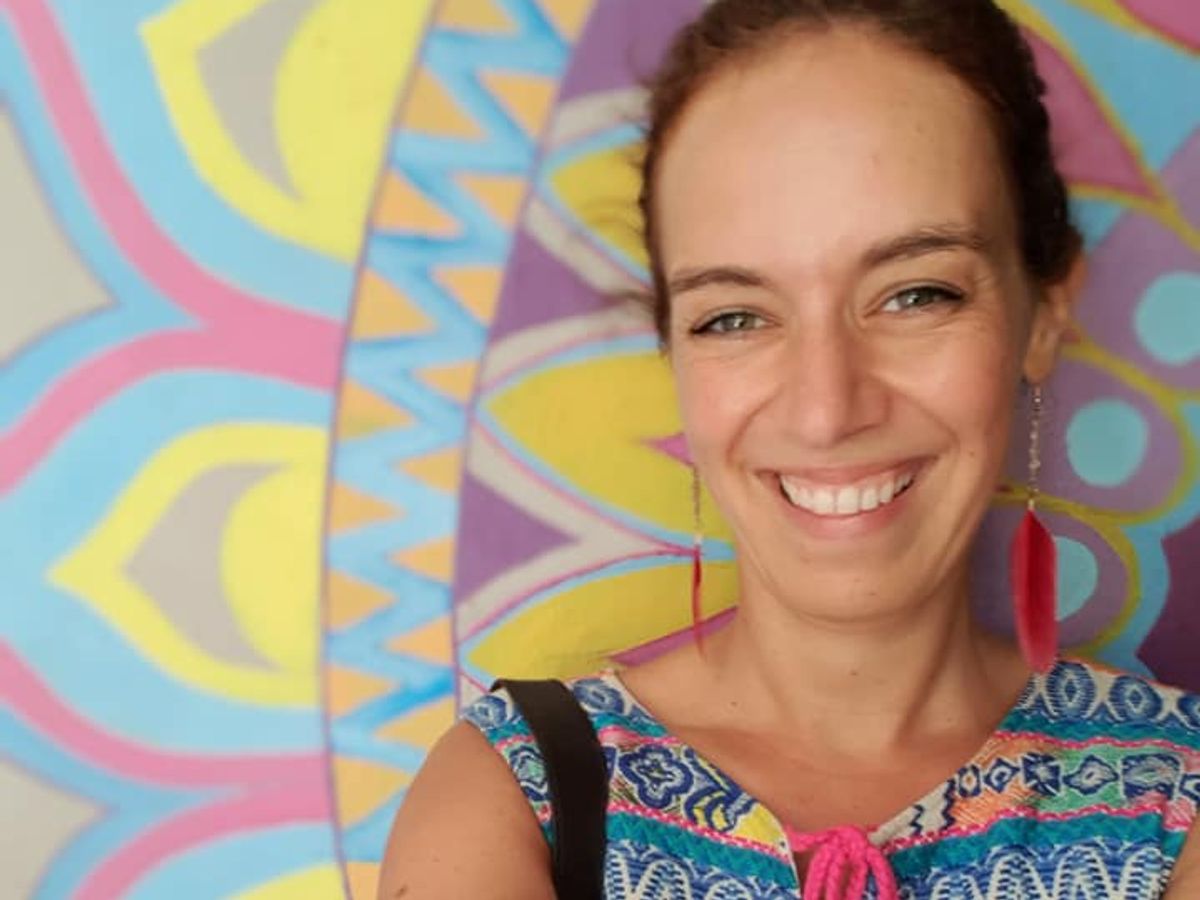 Janie Petersen lachend tegen een muur in het zonlicht