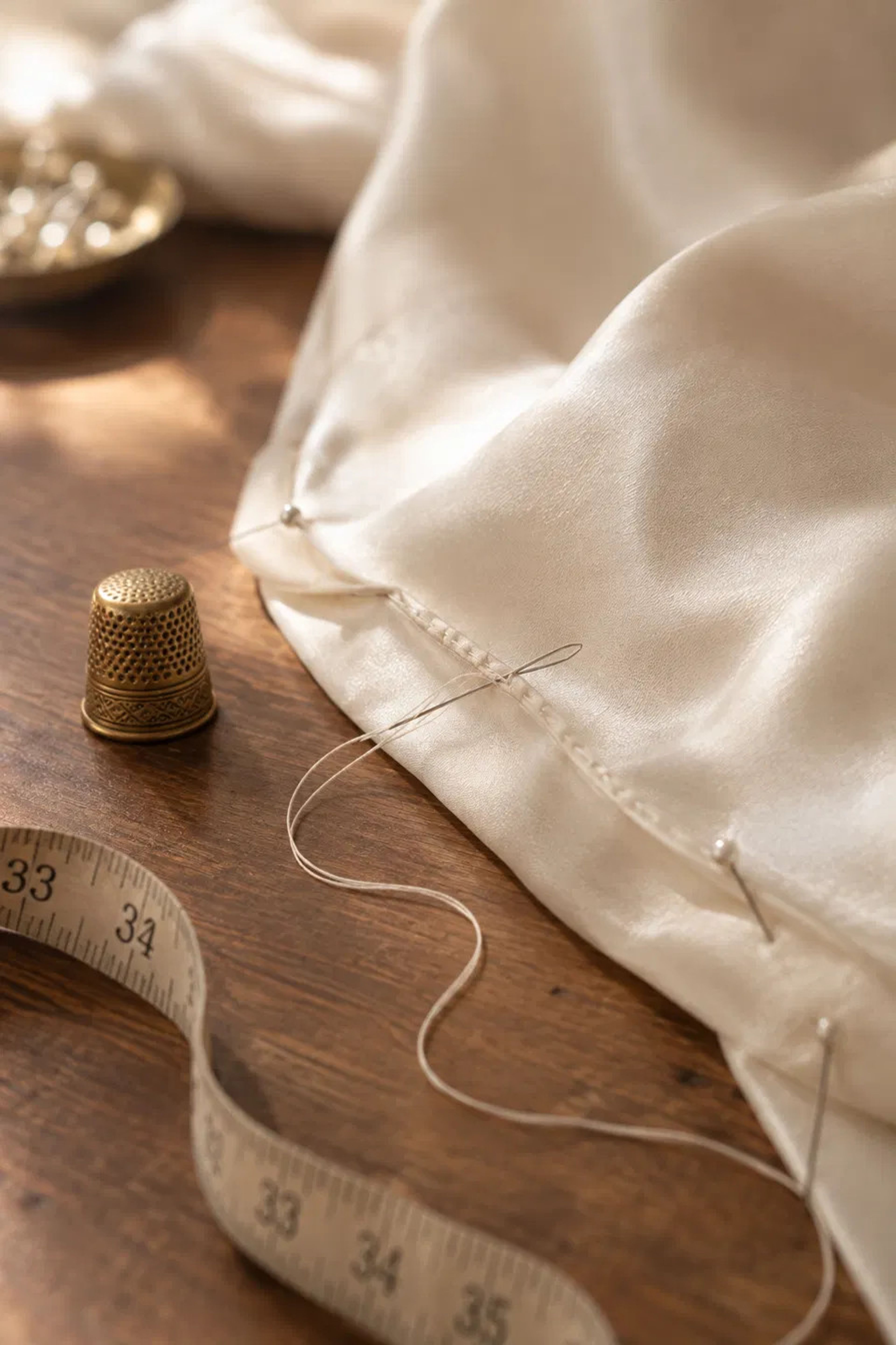 Hand-stitched blind hem on ivory silk with a brass thimble and tape measure