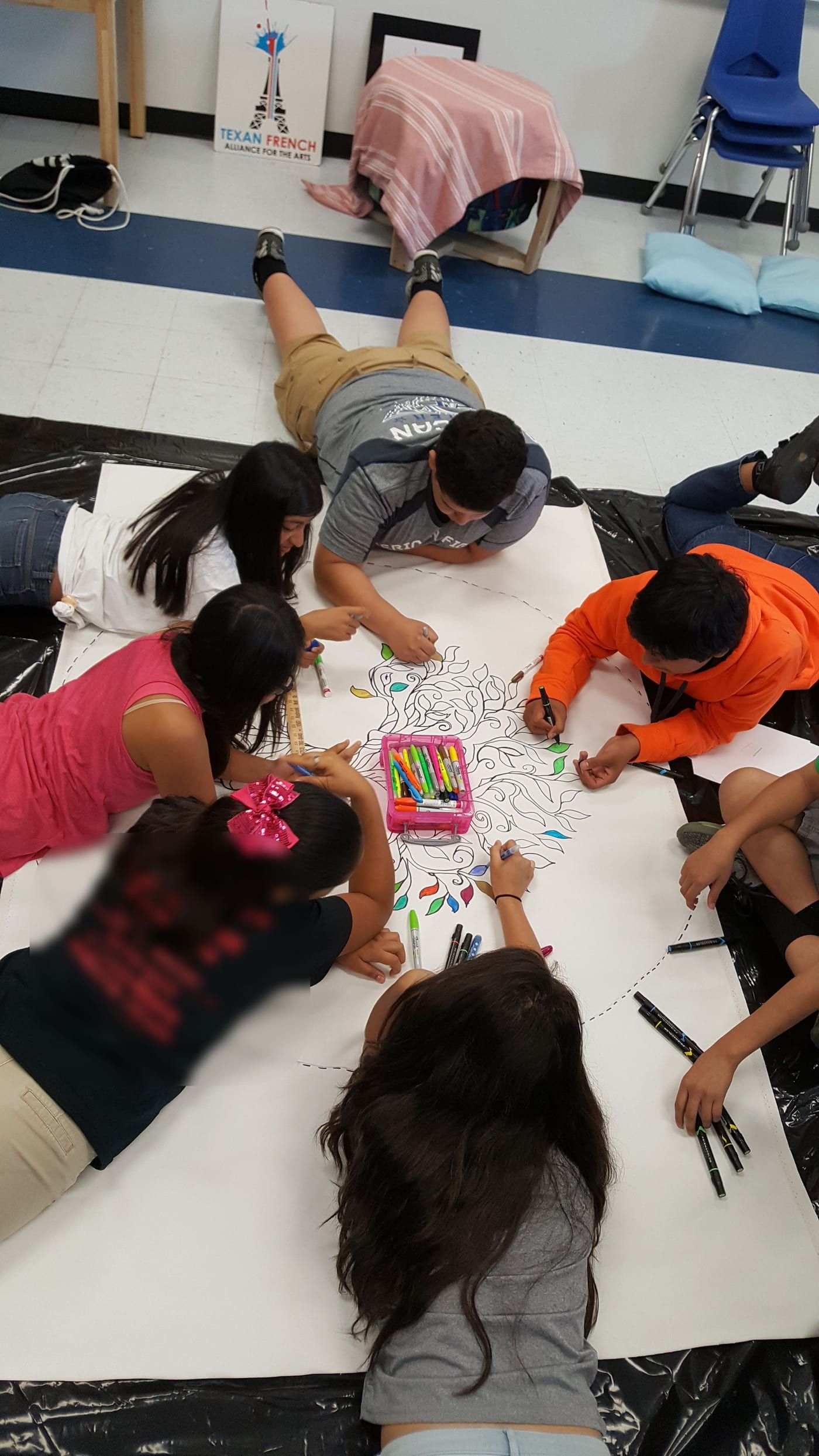 Students lying on the floor together, coloring a large drawing of a tree