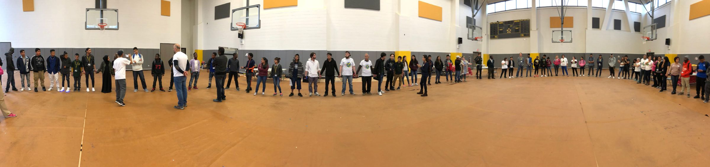 Young people and facilitators holding hands in a large circle in a school gym