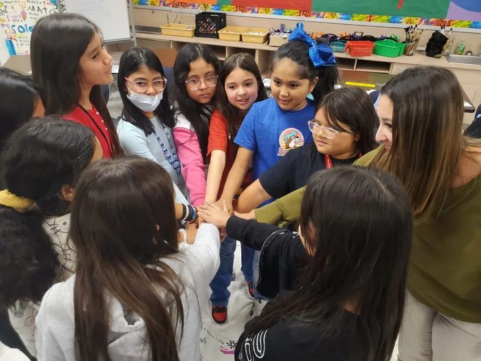Students and a facilitator stacking their hands together in a huddle