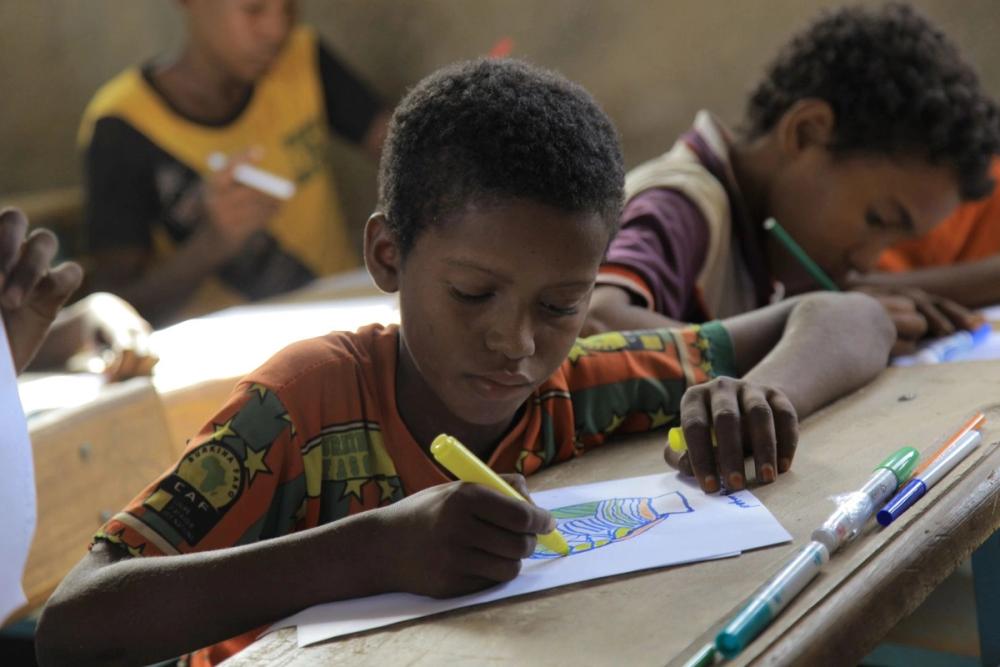A boy in a refugee camp school drawing with a yellow marker