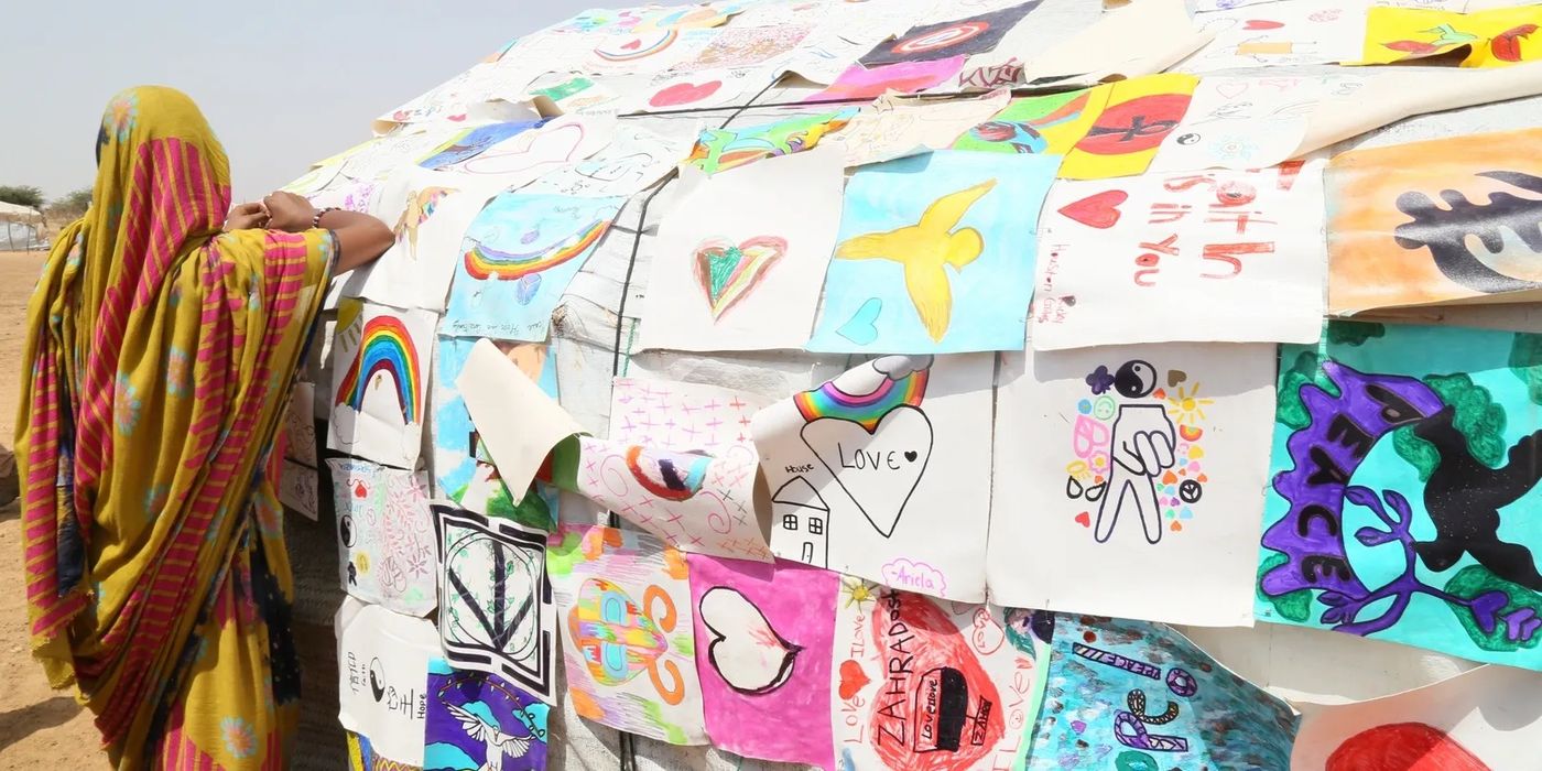 A woman beside a tent covered in children’s paintings of hope