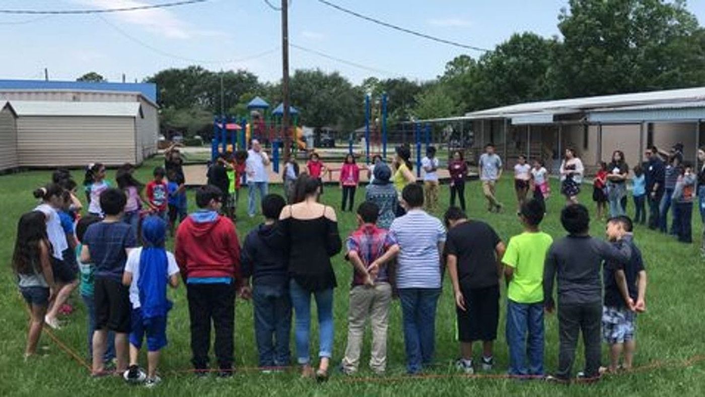 Children and facilitators standing in a circle on a school field