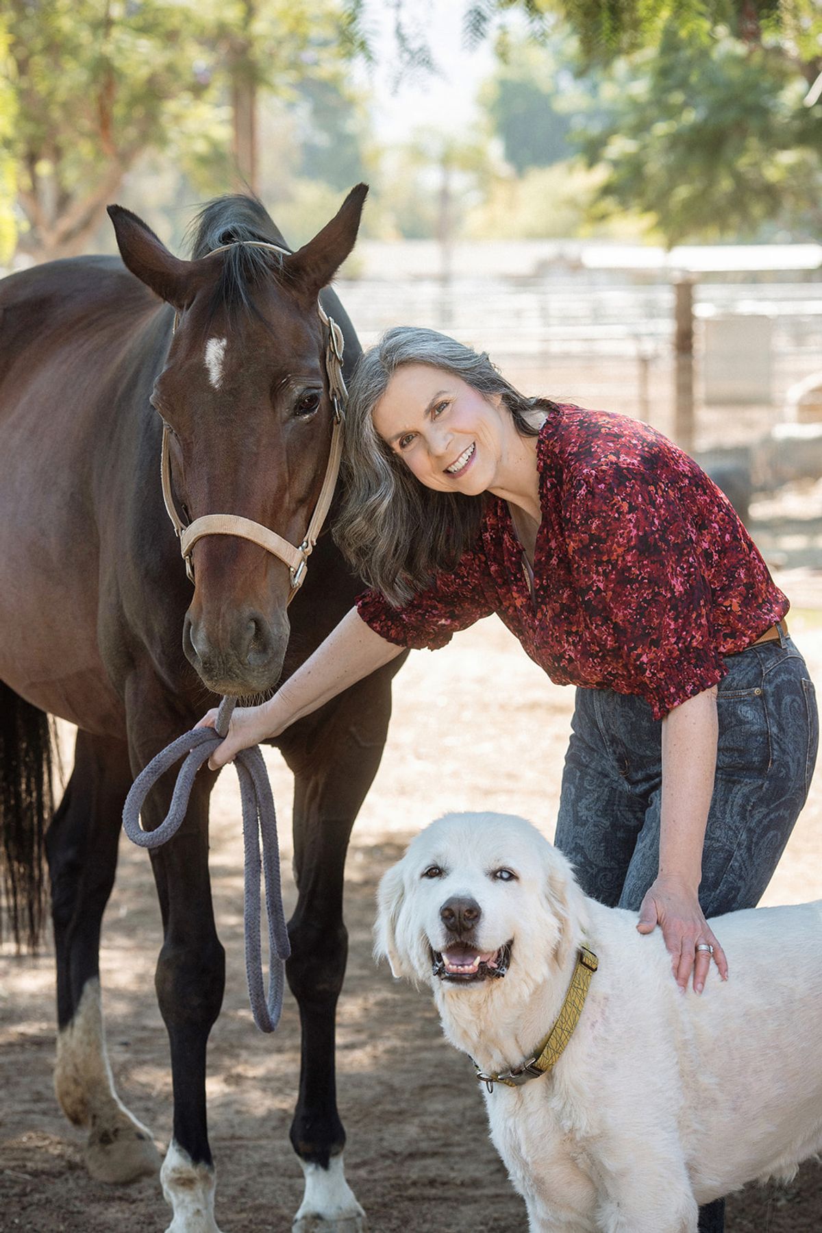 Photographer Kelly McNamara holding the lead rope for a bay horse while petting a big white dog