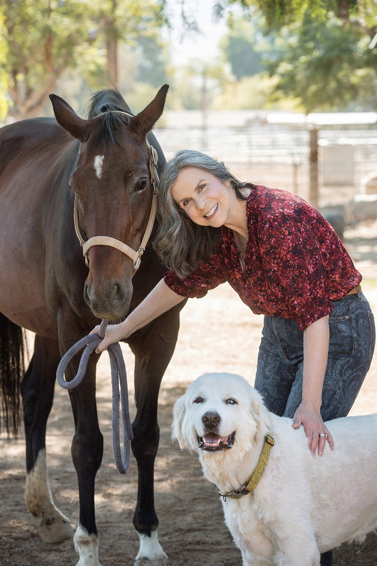 Kelly Mac holding a horse and a dog during a photoshoot at a barn