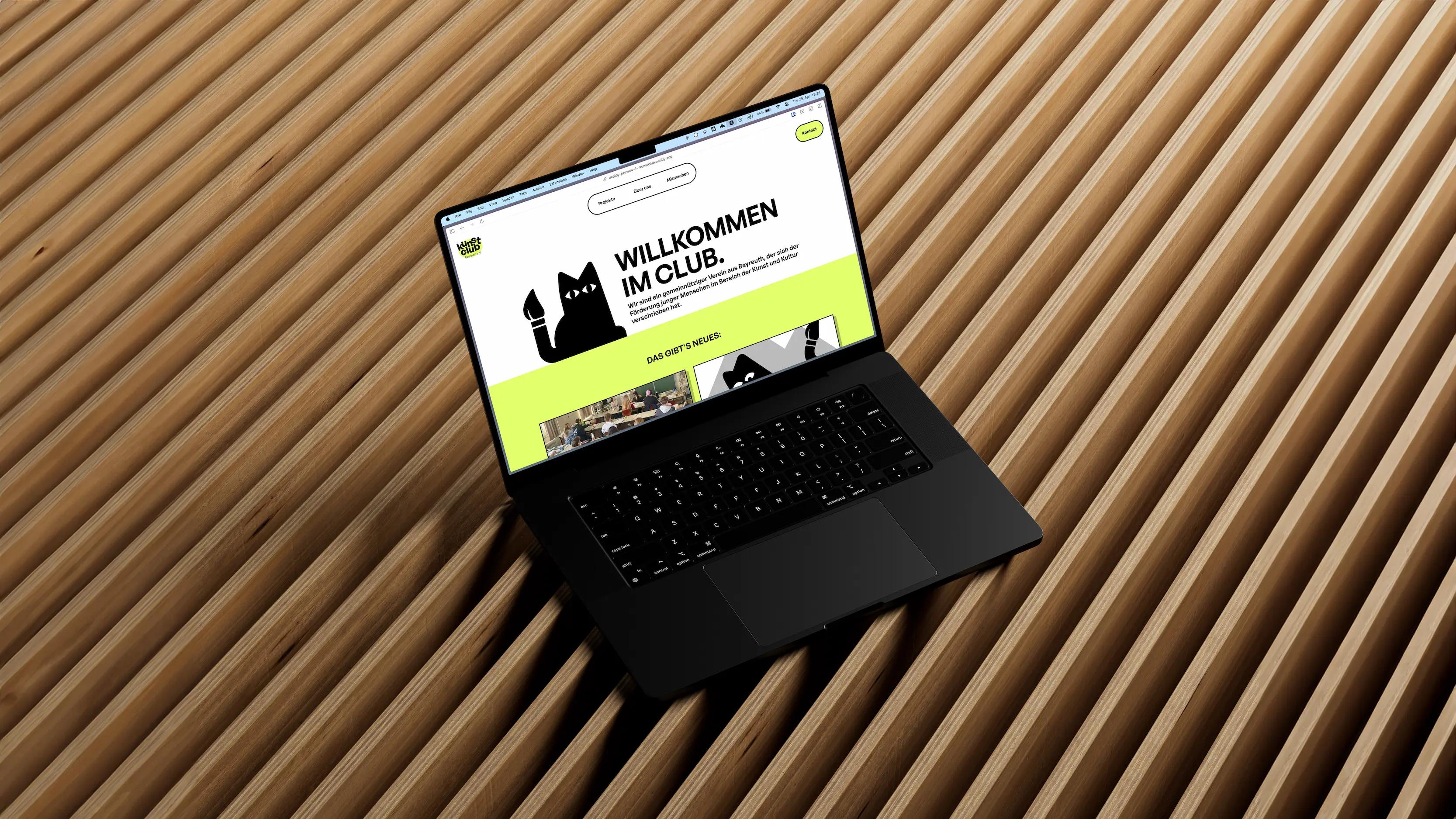 Mockup eines MacBooks auf einem Holzuntergrund. Der Bildschirm zeigt die Homepage des Kunstclub Bayreuth e.V.