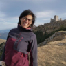 a woman wearing glasses and a purple jacket smiles in front of a castle