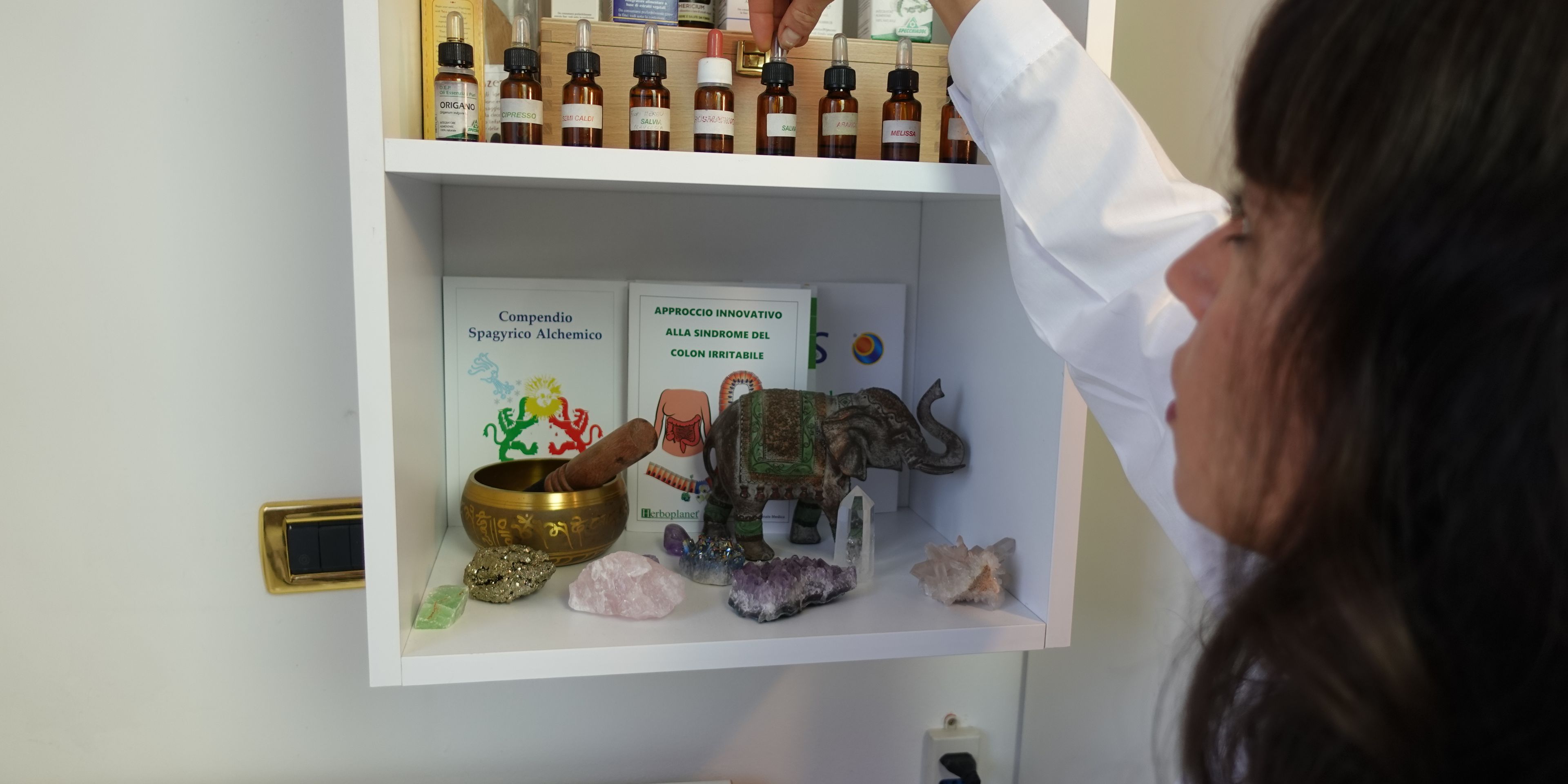 a woman is reaching for a bottle of essential oil on a shelf .