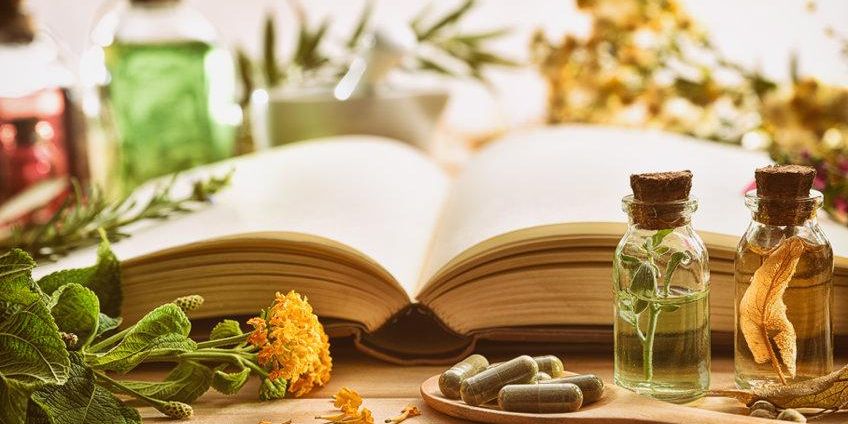 a wooden table topped with a book , bottles of herbs and pills .
