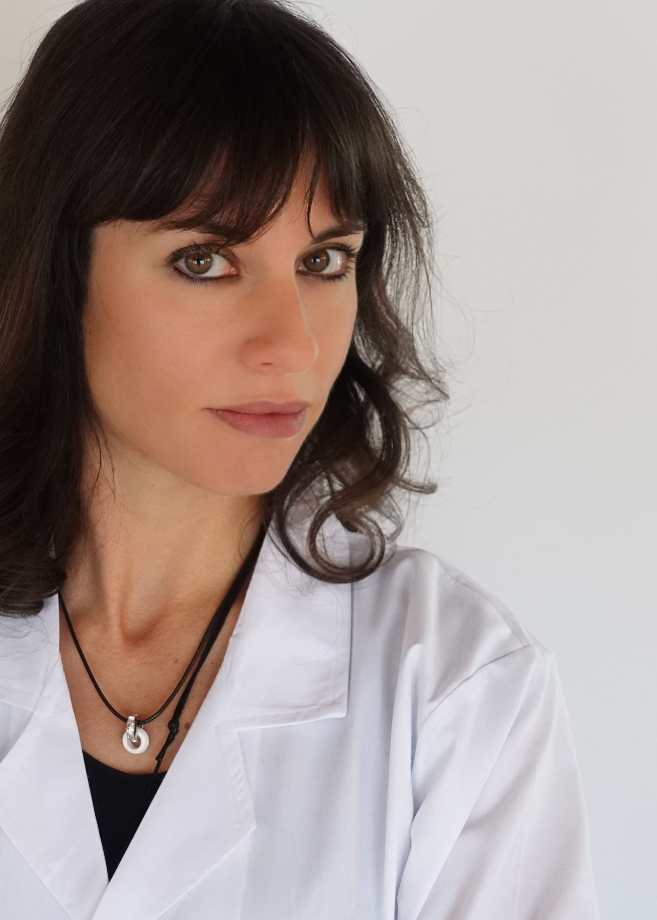 a woman in a white lab coat and necklace is looking at the camera .