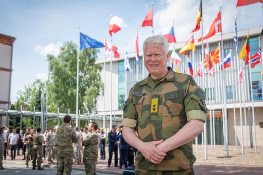 Portrett av en millitær leder, utendørs. I uniform, på en offentlig plass. Bak henger flere europeiske flagg.