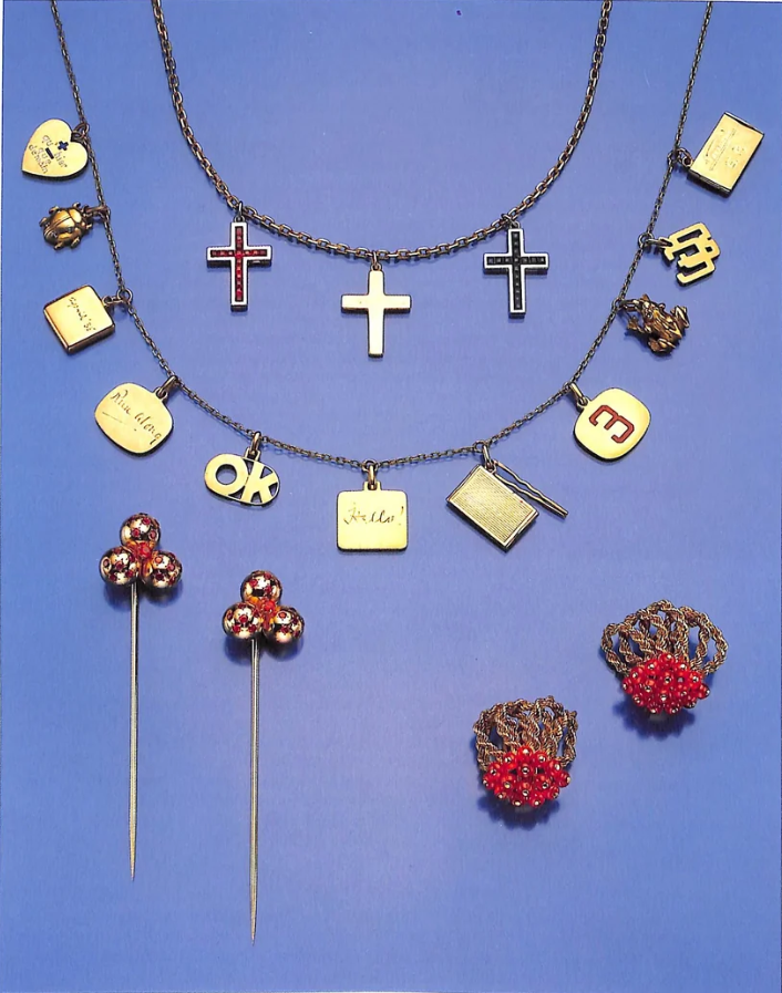 A group of gold charms, hairpins, and gem-set button earrings from the 1987 Sotheby's sale catalogue, including cross- and heart-shaped charms, a ladybird, and cabochon-ruby cluster hairpins.