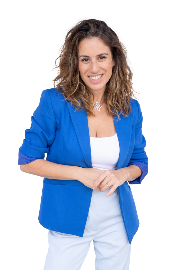 עידית גבע מחייכת, לובשת ז׳קט כחול מעל חולצה לבנה