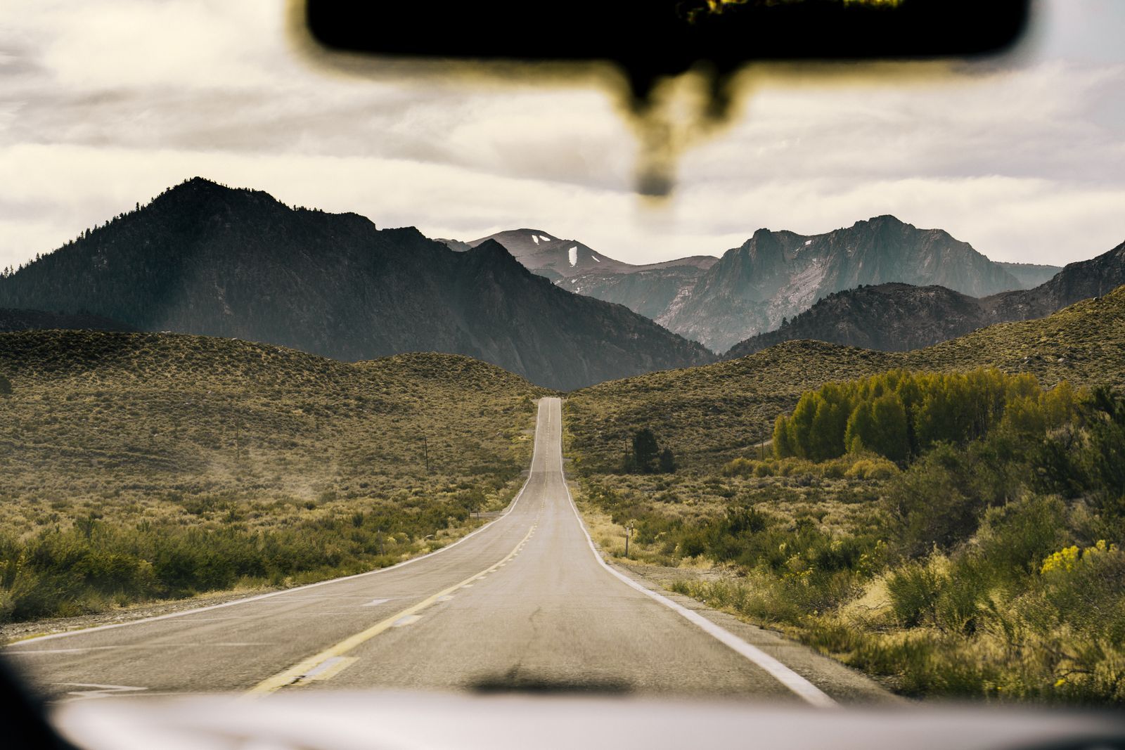 An open highway stretching through mountainous countryside seen through a car windshield, evoking a long relocation journey