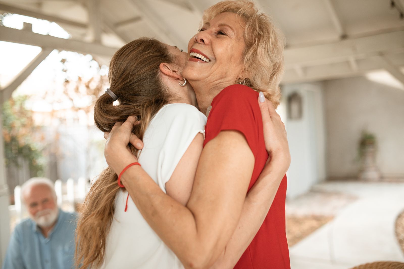 An adult daughter warmly embraces her smiling elderly mother during a visit at home