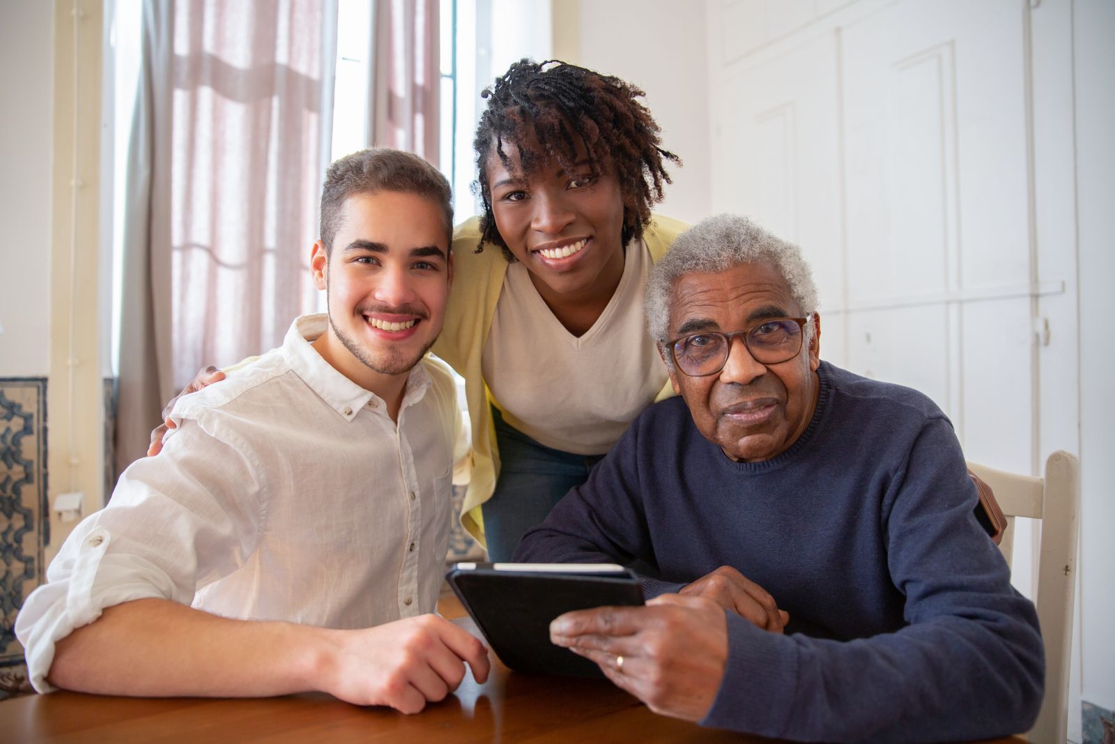 A multigenerational family of an adult son, daughter, and senior father gather warmly at home to research senior living options together