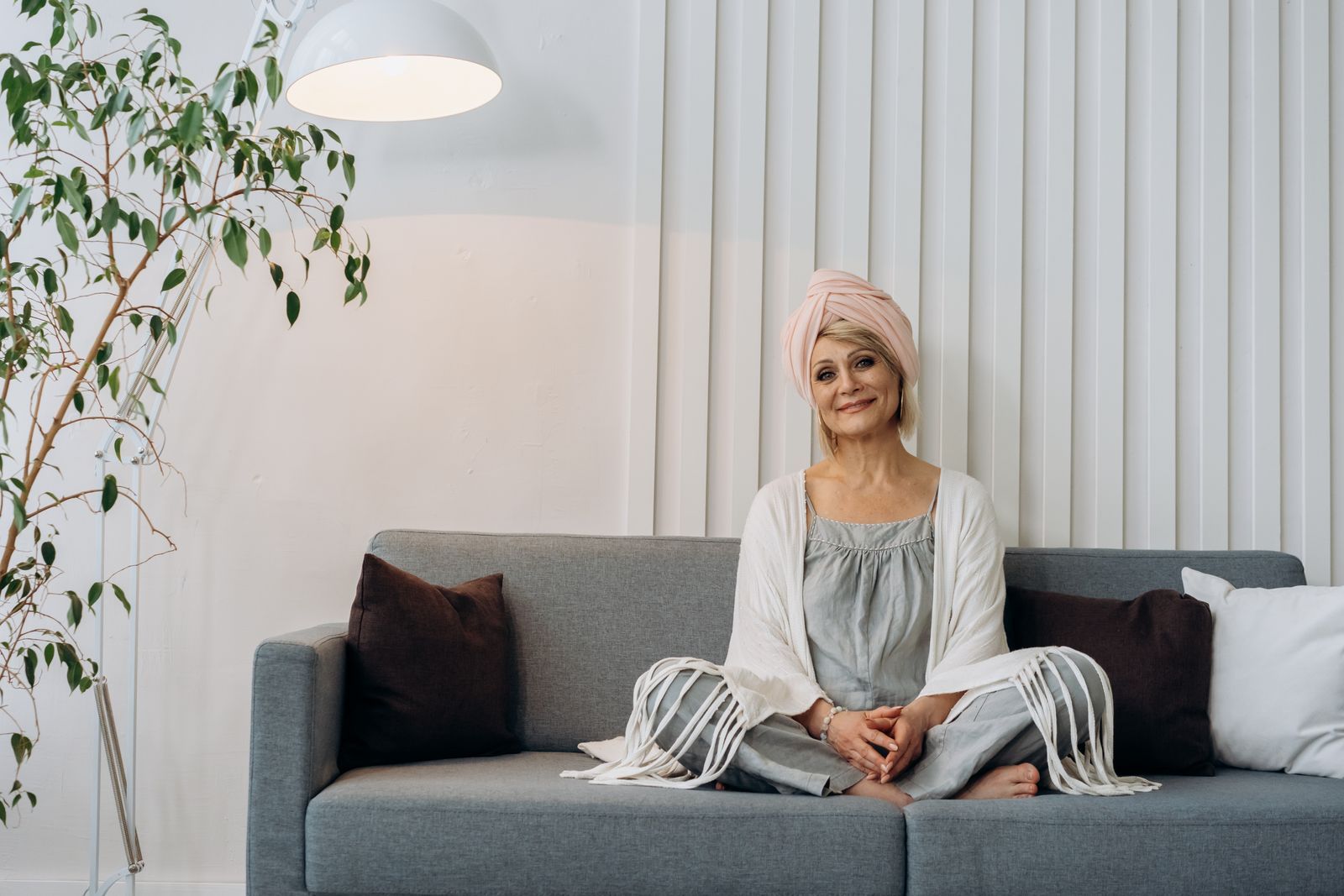A smiling senior woman in a head wrap relaxes comfortably on a sofa in a bright, welcoming living room