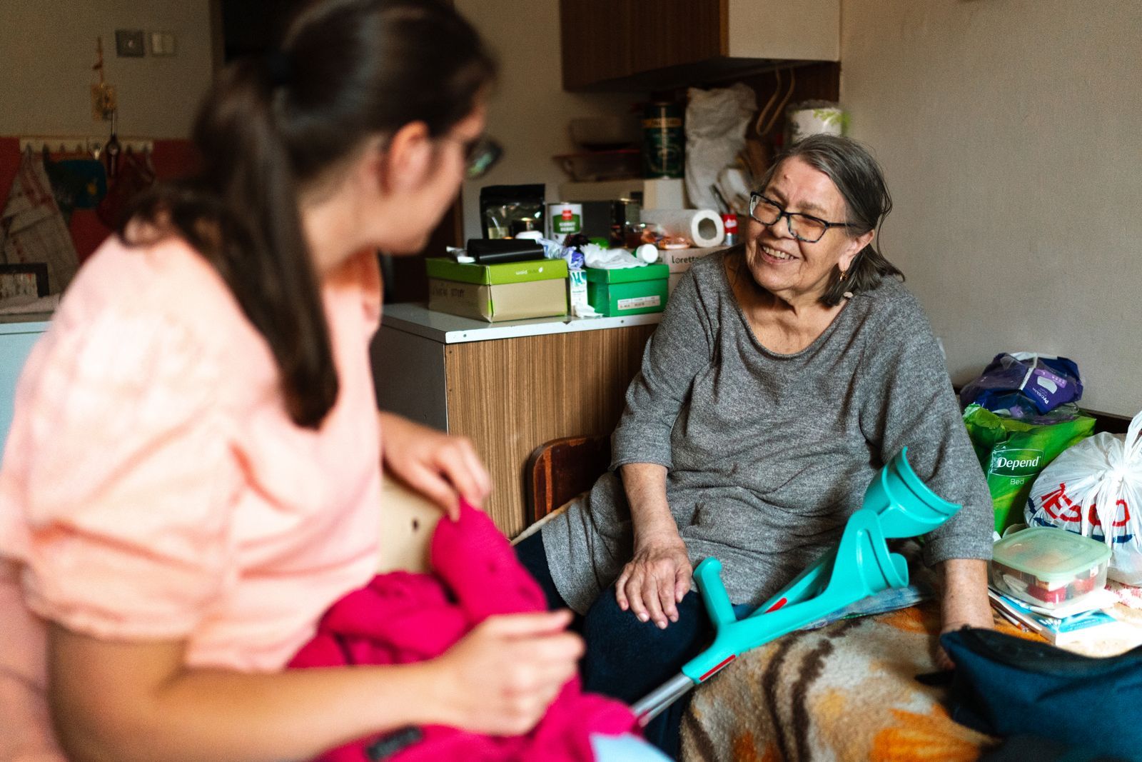 A home caregiver shares a warm, smiling moment with a senior woman using forearm crutches in her living room